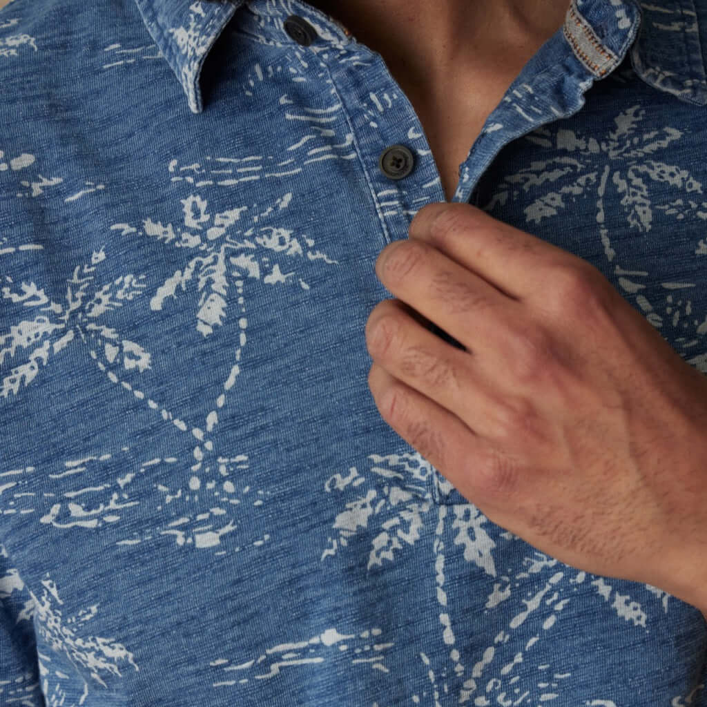 Close-up of a man adjusting the collar of a dark indigo printed polo shirt with a tropical design.