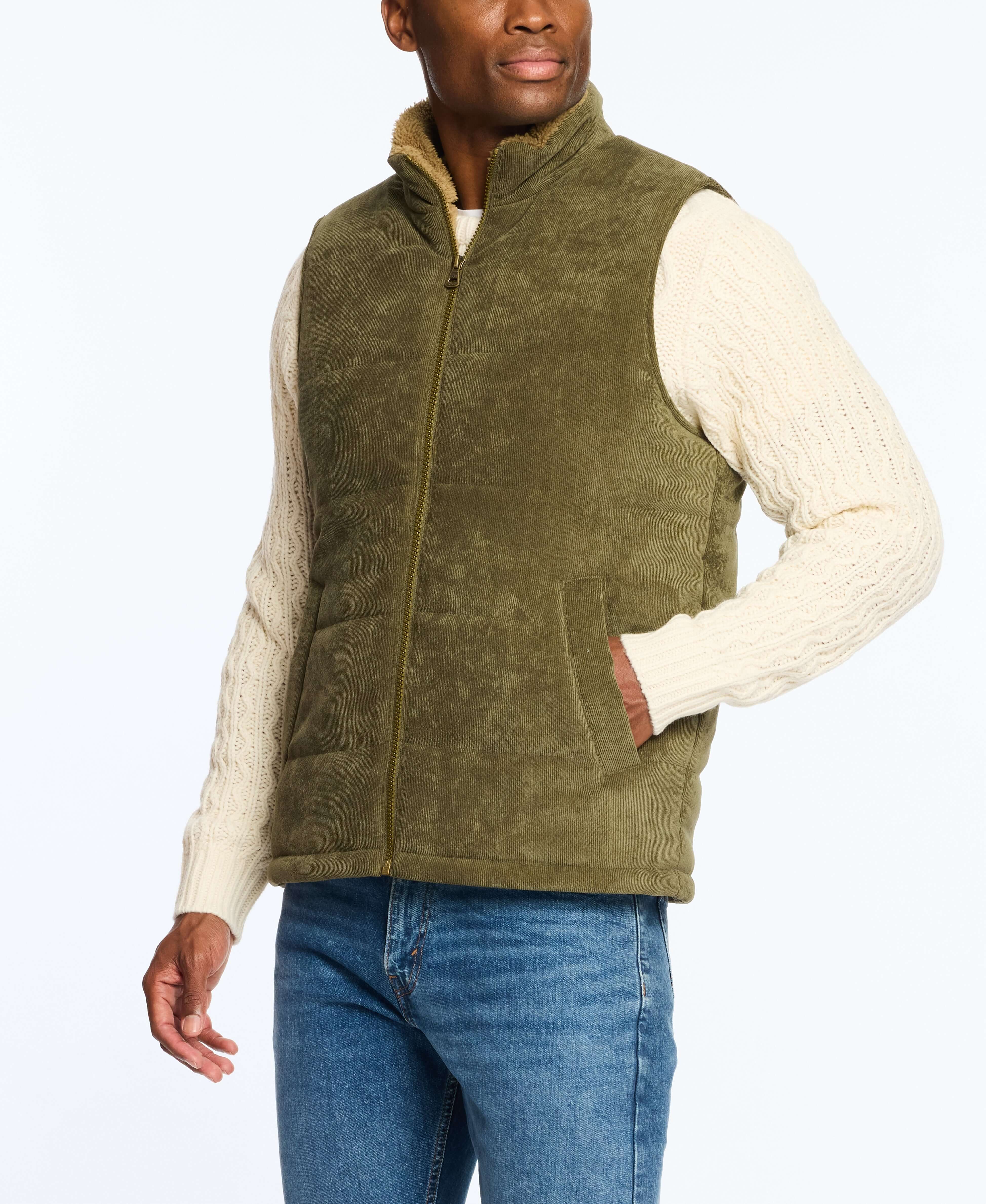 Man wearing a corded puffer vest in olive with shearling lining, paired with a cream sweater and jeans.