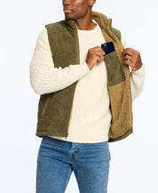 Man wearing olive corded puffer vest lined with shearling, showcasing side pockets, paired with a cream sweater.