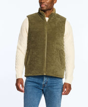 Man wearing an olive corded puffer vest with shearling lining, paired with a cream cable-knit sweater.