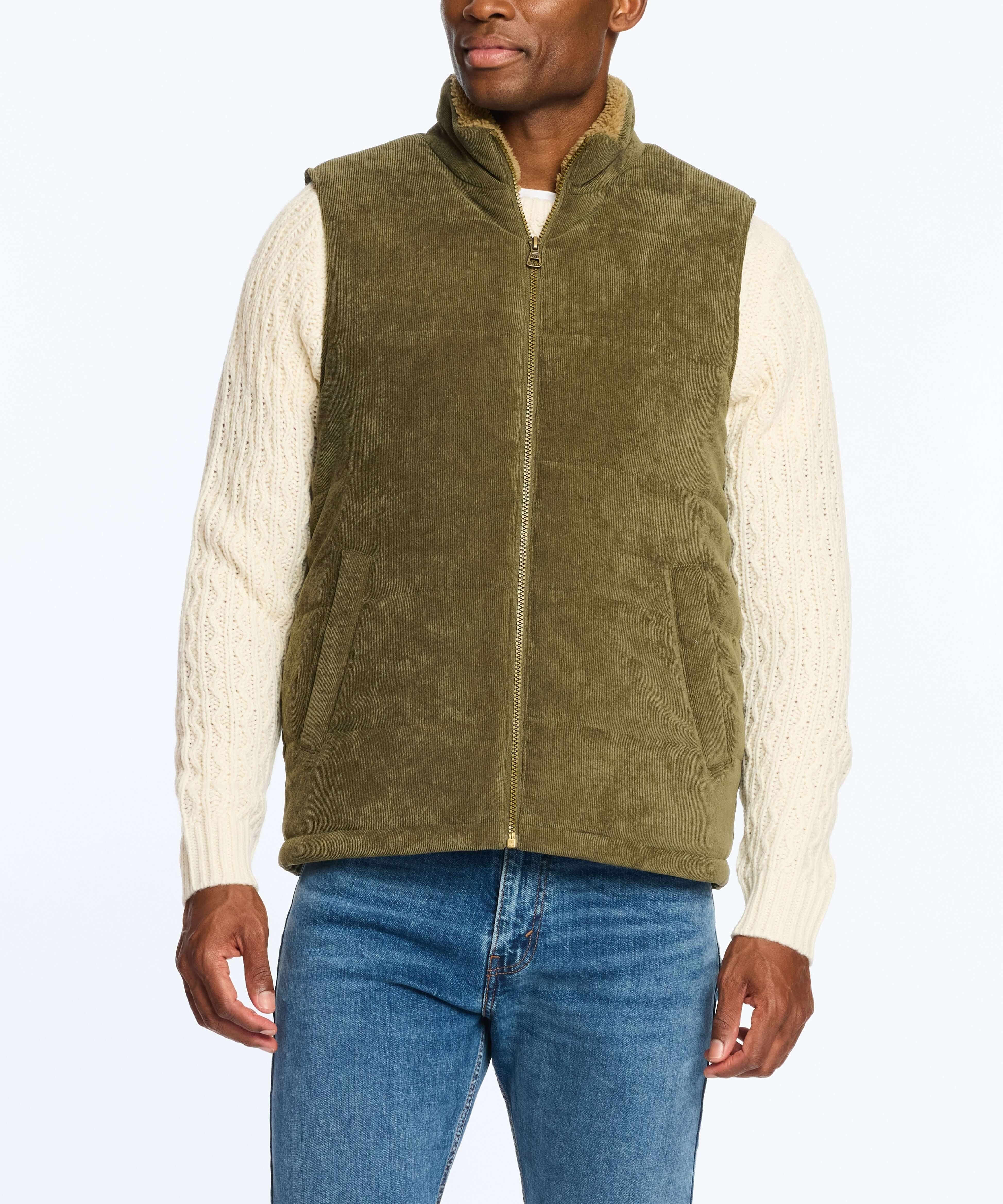 Man wearing an olive corded puffer vest with shearling lining, paired with a cream cable-knit sweater.