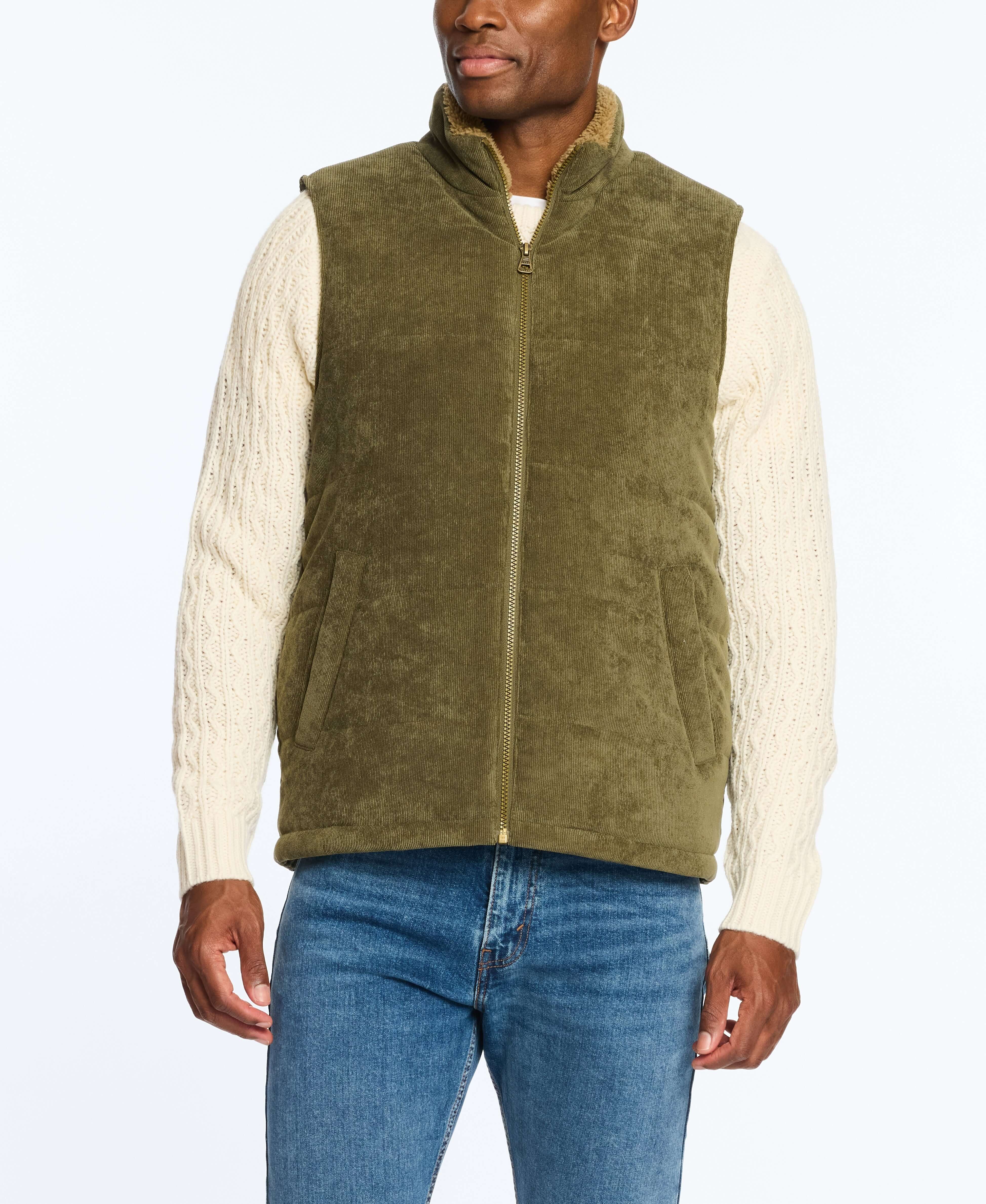 Man wearing an olive corded puffer vest with shearling lining, paired with a cream cable-knit sweater.