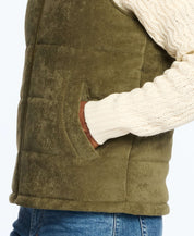 Side view of an olive corded puffer vest with shearling lining, paired with a cozy cream sweater and denim.