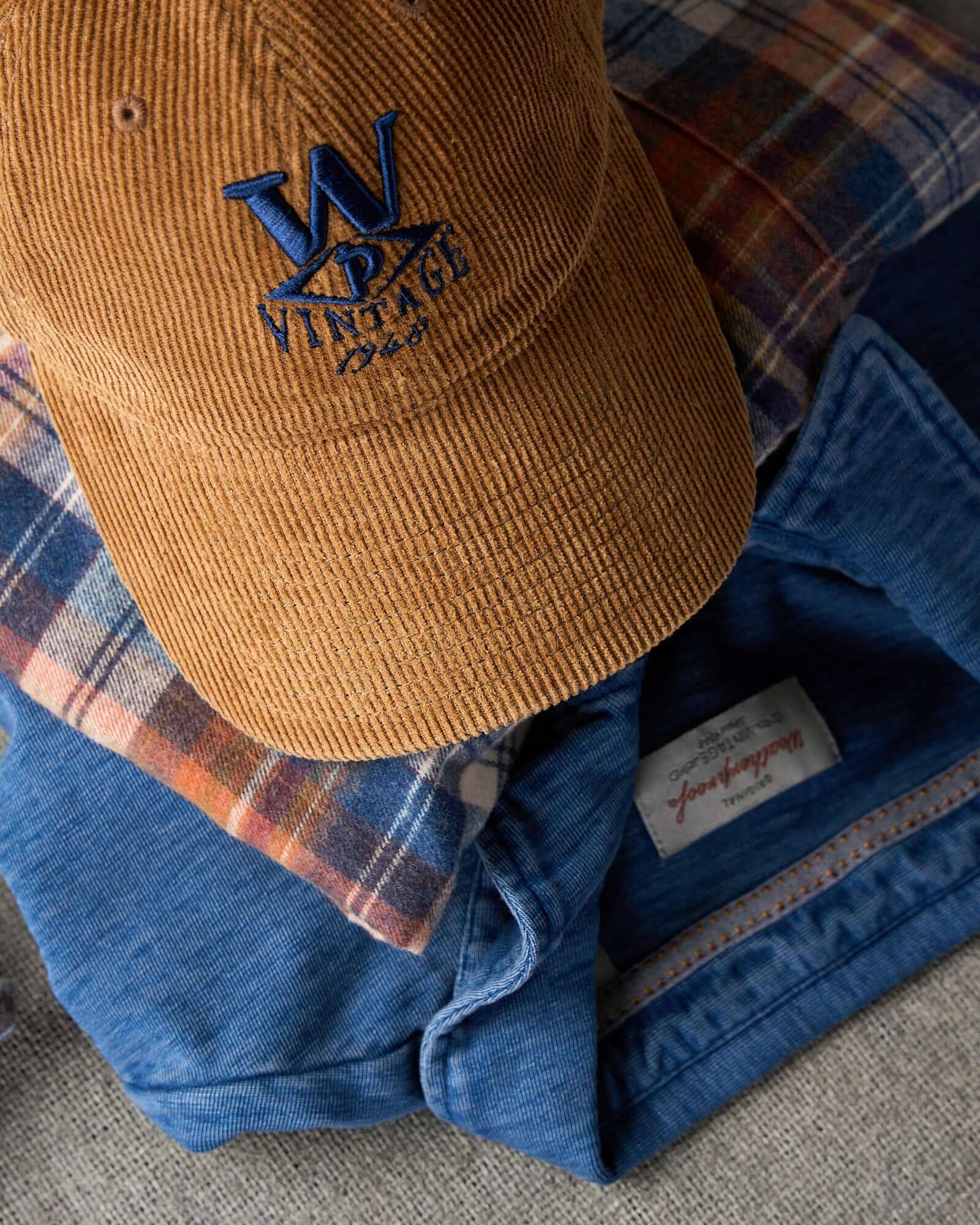 Corduroy Relaxed Hat in Brown on top of a plaid shirt and a blue jacket, perfect for staying warm and stylish.
