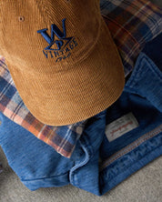 Corduroy Relaxed Hat in Brown on top of a plaid shirt and a blue jacket, perfect for staying warm and stylish.