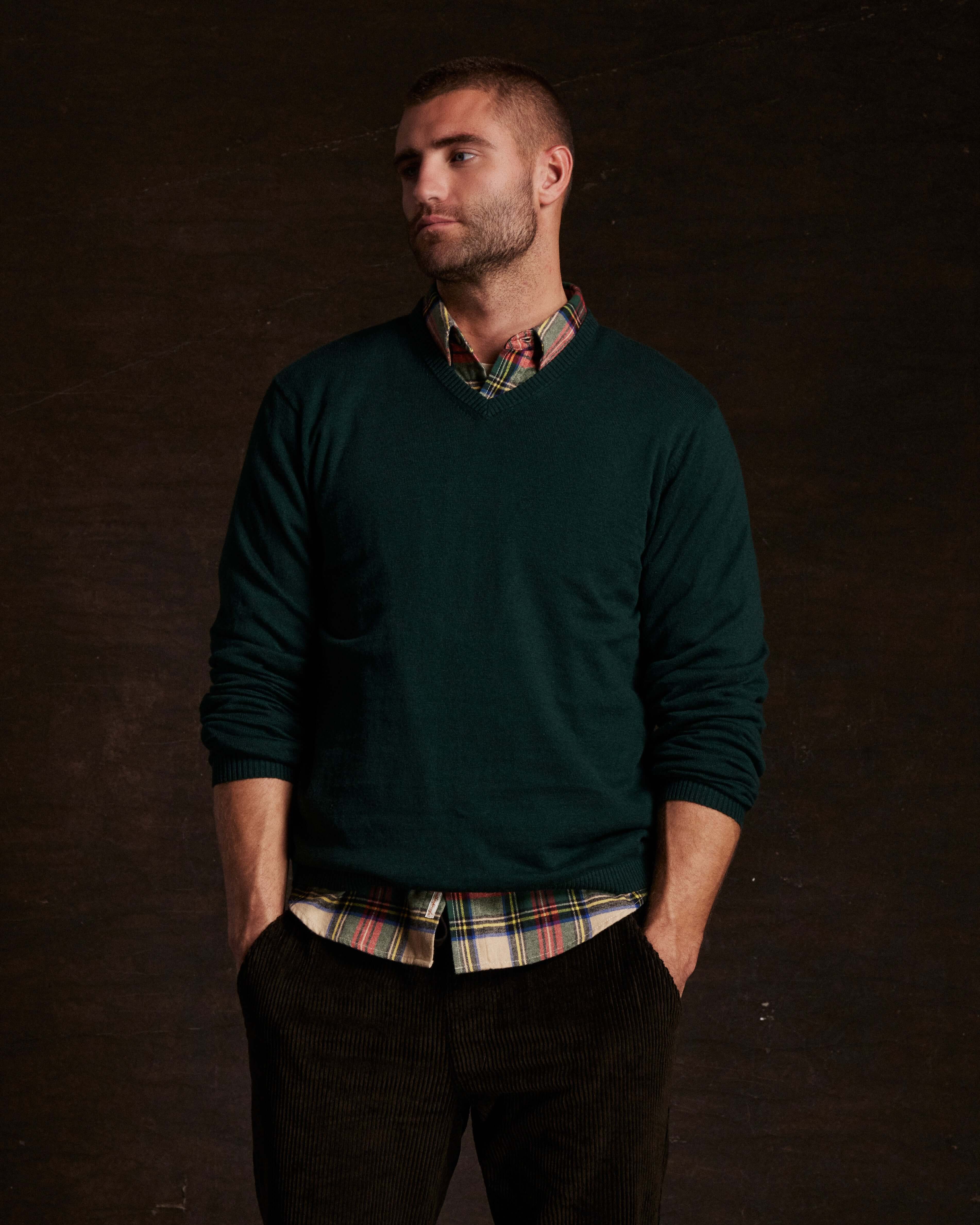 Cotton cashmere holiday v-neck sweater in pine, styled casually over a plaid shirt, modeled by a man.