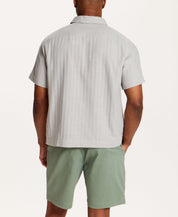 Back view of a man wearing the Cotton Gauze Herringbone Polo in Vapor Grey with green shorts.