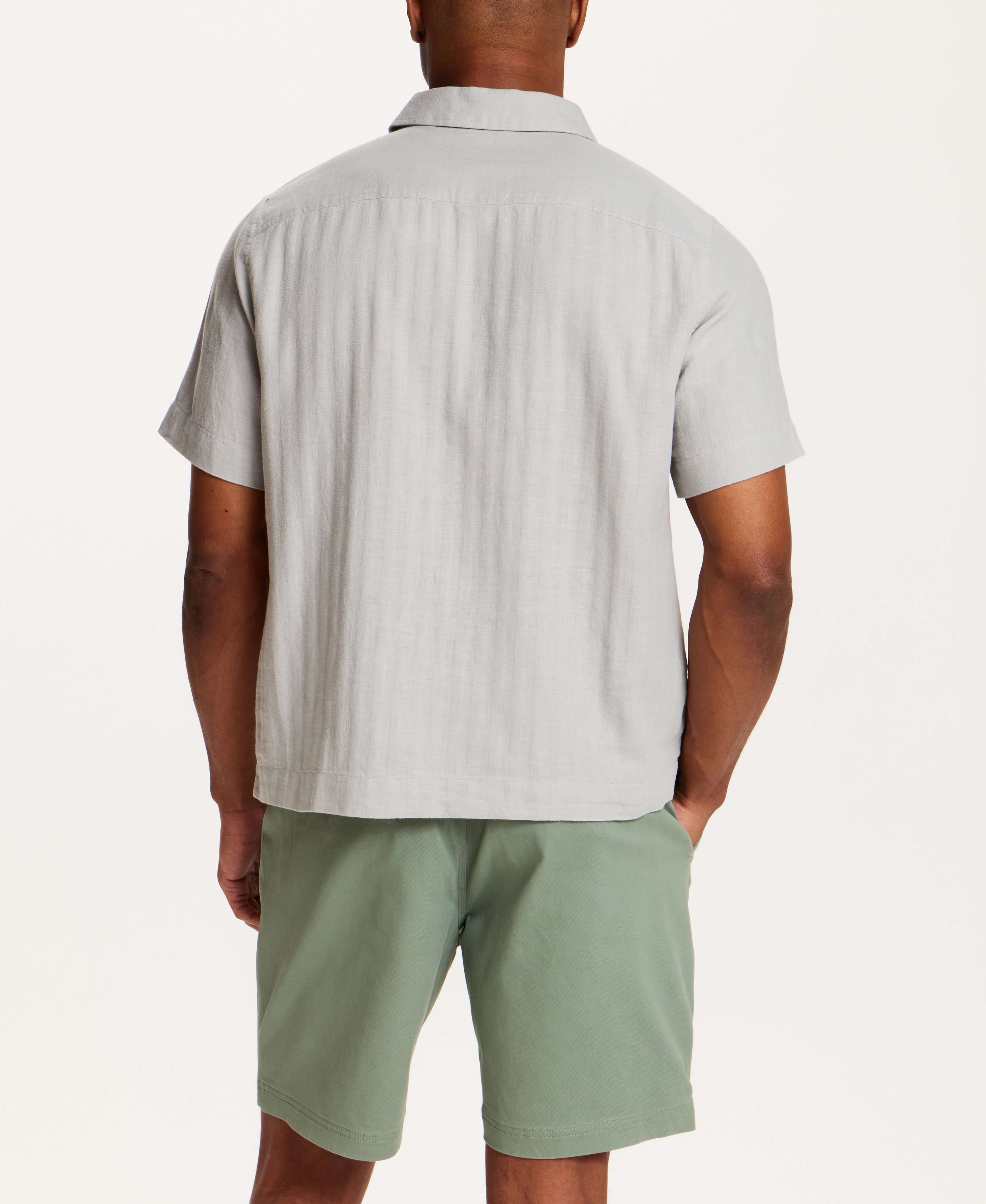 Back view of a man wearing the Cotton Gauze Herringbone Polo in Vapor Grey with green shorts.