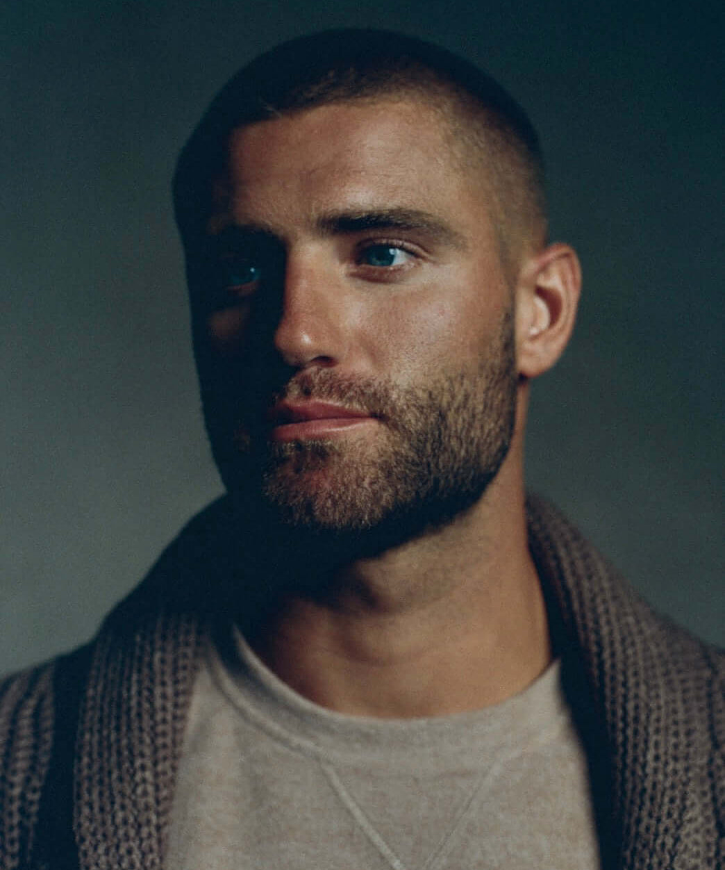 Close-up portrait of a man with short hair and a beard, wearing a cozy sweater and looking thoughtfully.