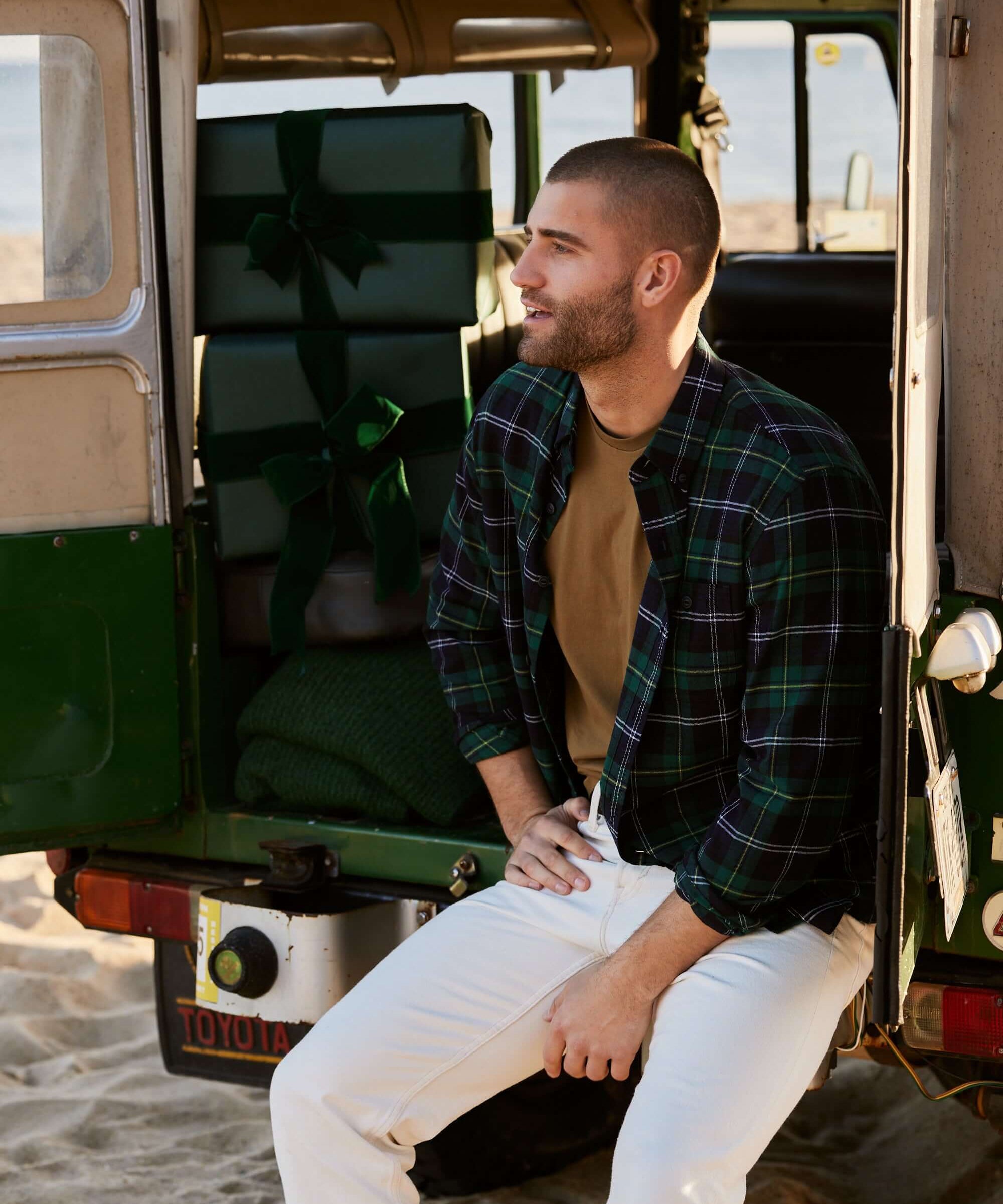 Model wearing Holiday Antique Flannel in Verdant Green, sitting in a vintage vehicle with holiday gifts.