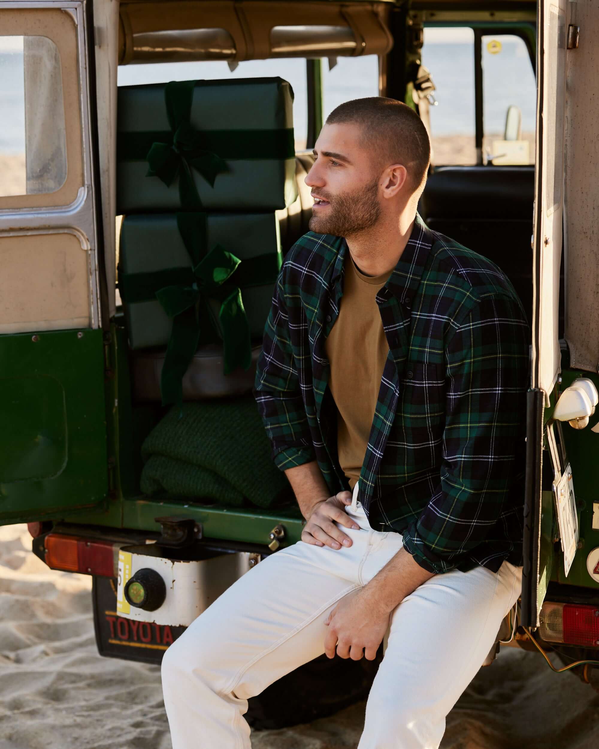 Model wearing Holiday Antique Flannel in Verdant Green, sitting in a vintage vehicle with holiday gifts.