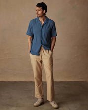 Man wearing a blue short-sleeve shirt and beige linen blend drawstring pants, showcasing a relaxed fit style.