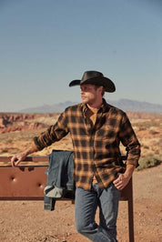 Man wearing Long Sleeve Brushed Flannel in Inca Gold, styled with a cowboy hat, against a rugged outdoor backdrop.