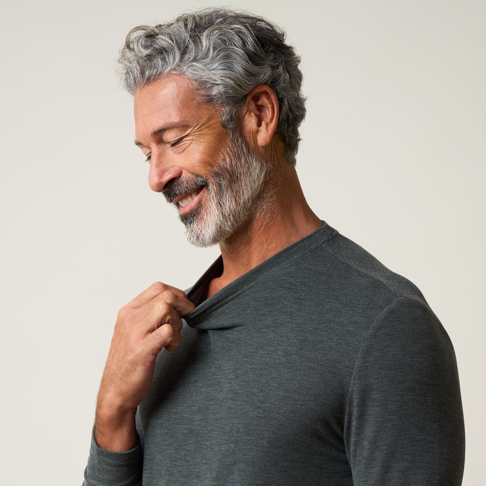 Close-up of a man smiling while adjusting the collar of a Long Sleeve Crew Neck in Charcoal.