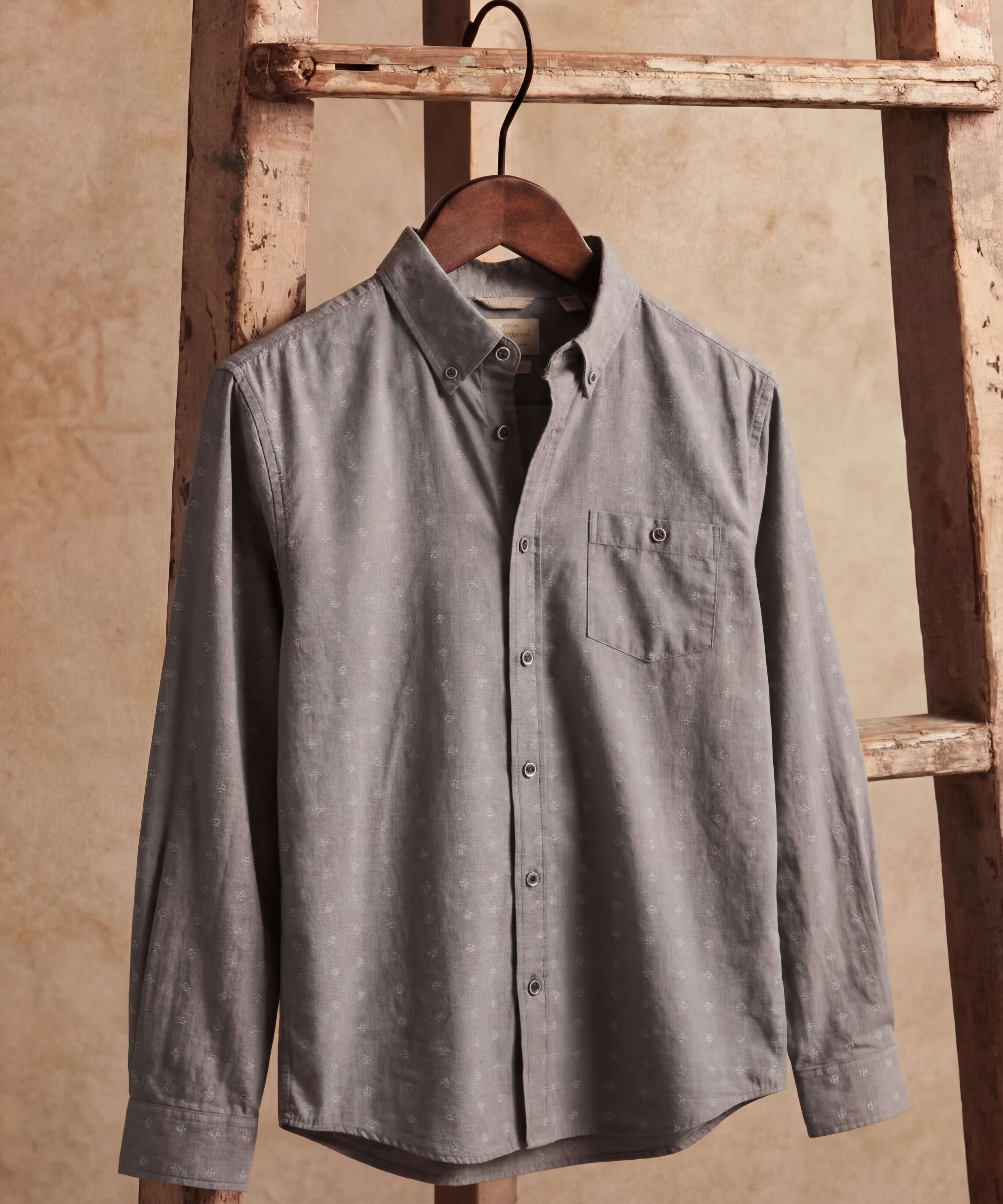 Long Sleeve Dobby Chambray in Moon Mist hanging on a wooden ladder, featuring jacquard dobby texture and button-front.