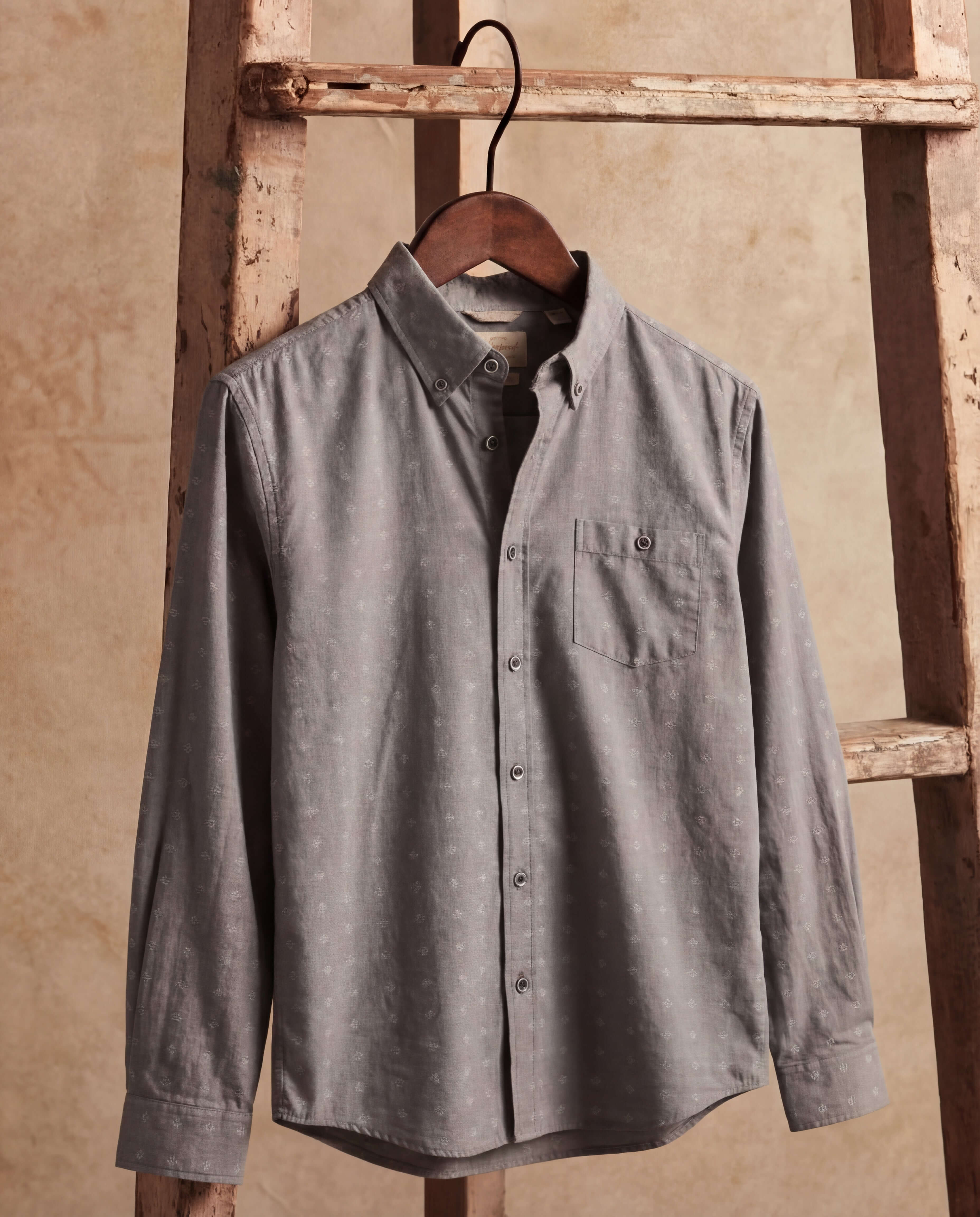 Long Sleeve Dobby Chambray in Moon Mist hanging on a wooden ladder, featuring jacquard dobby texture and button-front.