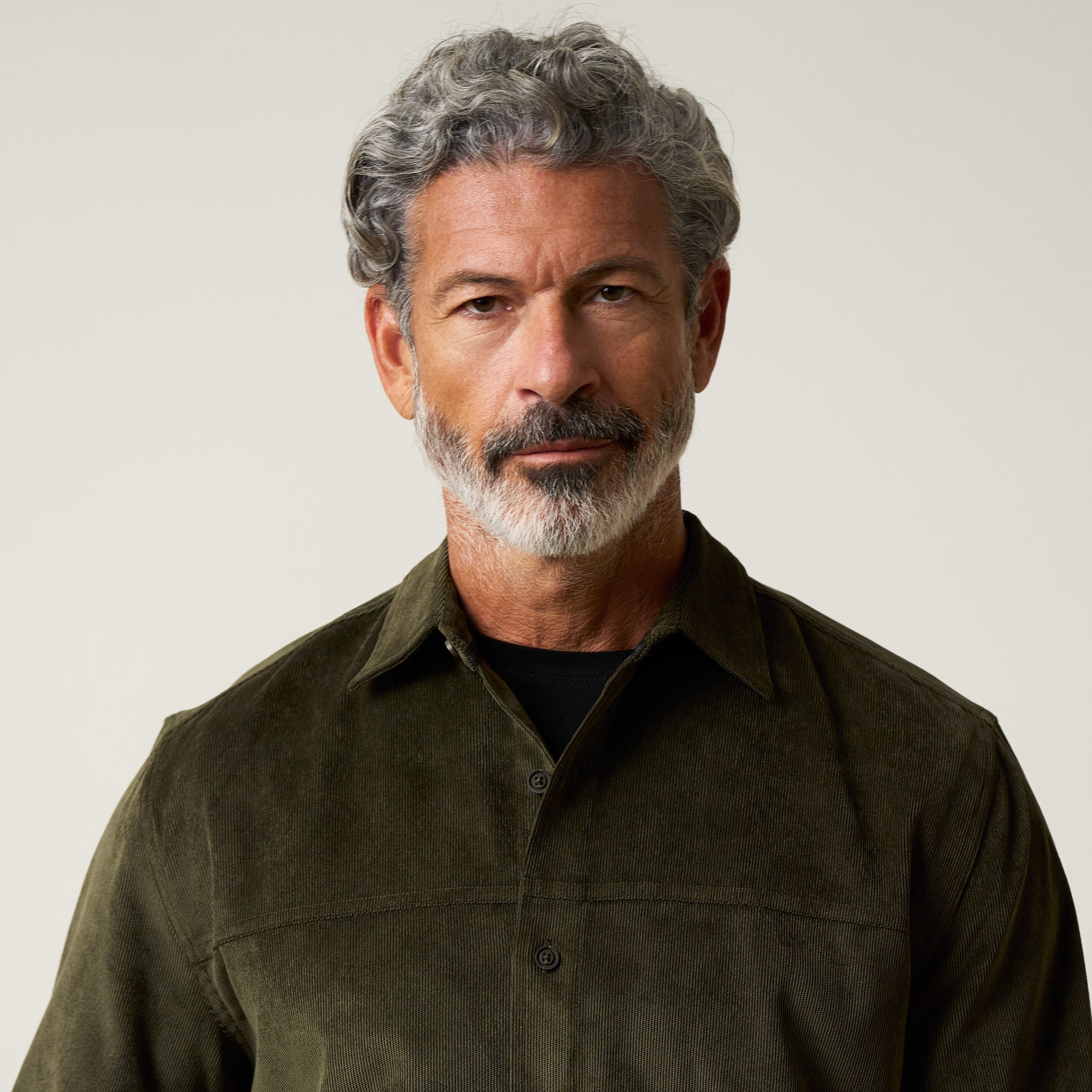 Long Sleeve Solid Cord Button Down in Olive modeled by a mature man with grey hair and a beard, wearing a corduroy shirt.