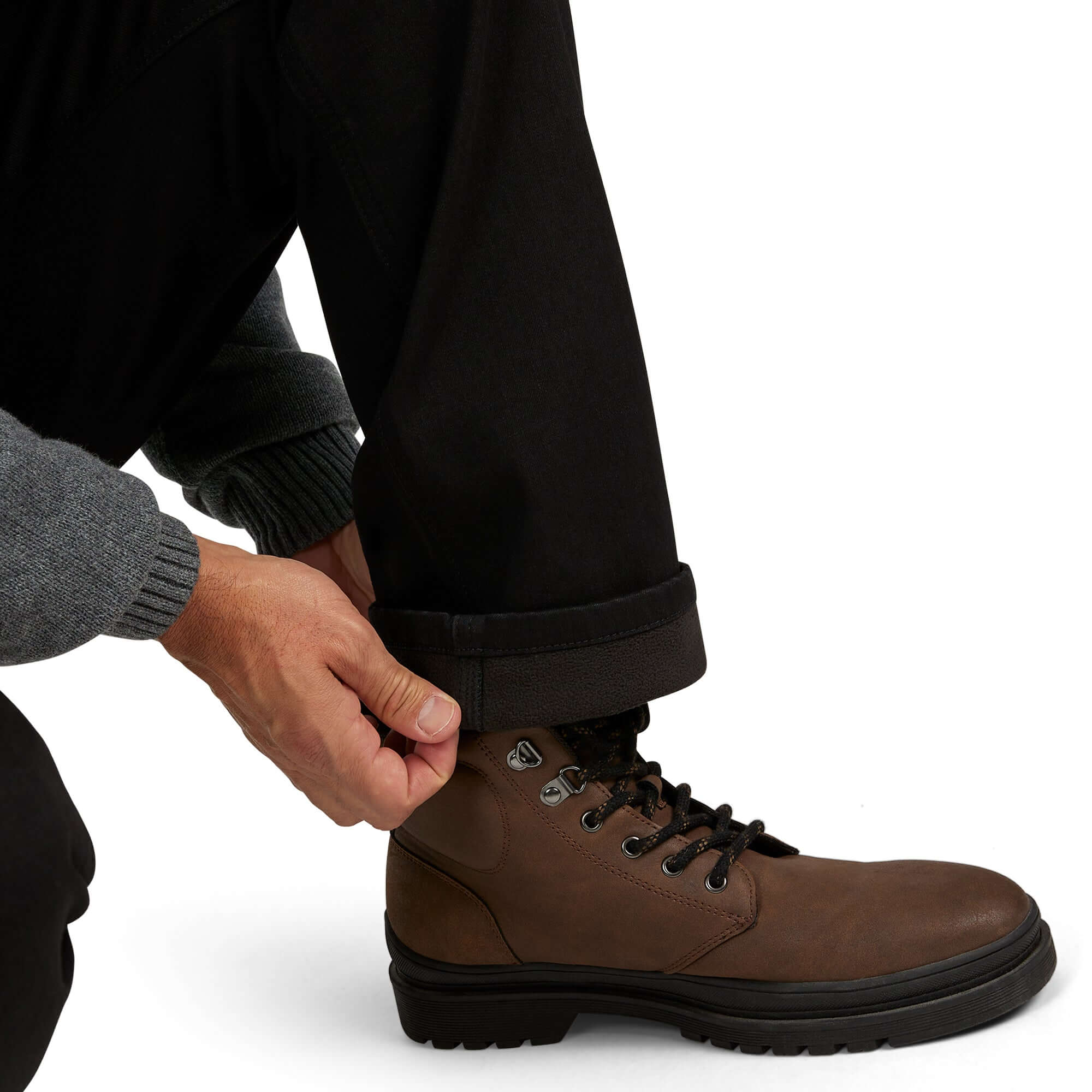 Person adjusting laces on brown boots while wearing regular fit fleece lined jeans and a grey sweater.