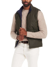 Matte Coated Shell Puffer Vest in Kambaba Olive worn by a model, styled with a knitted sweater and white pants.