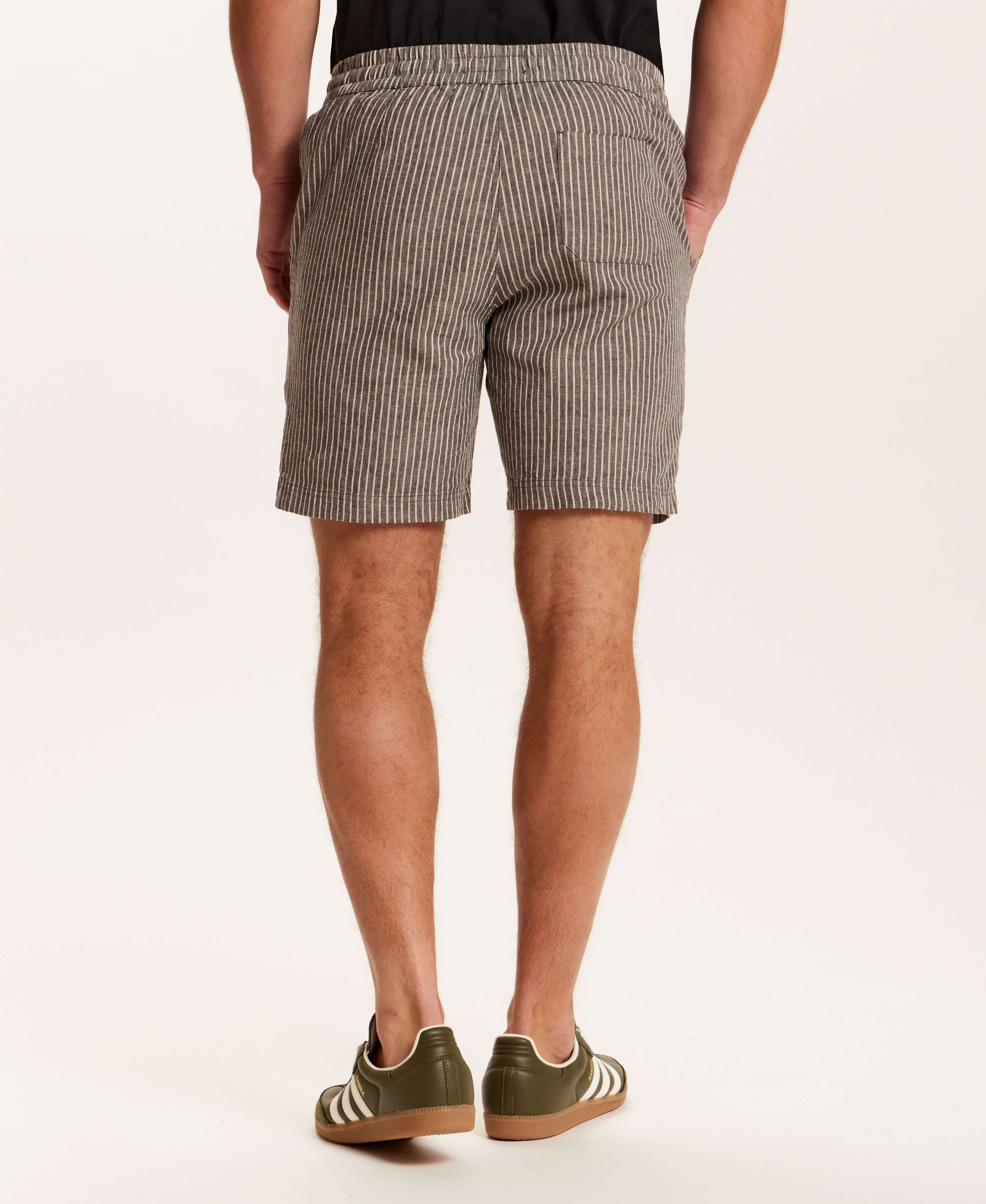 Back view of a man wearing Chambray Stripe Drawstring Short in Black Stripe with a striped pattern and side pockets.