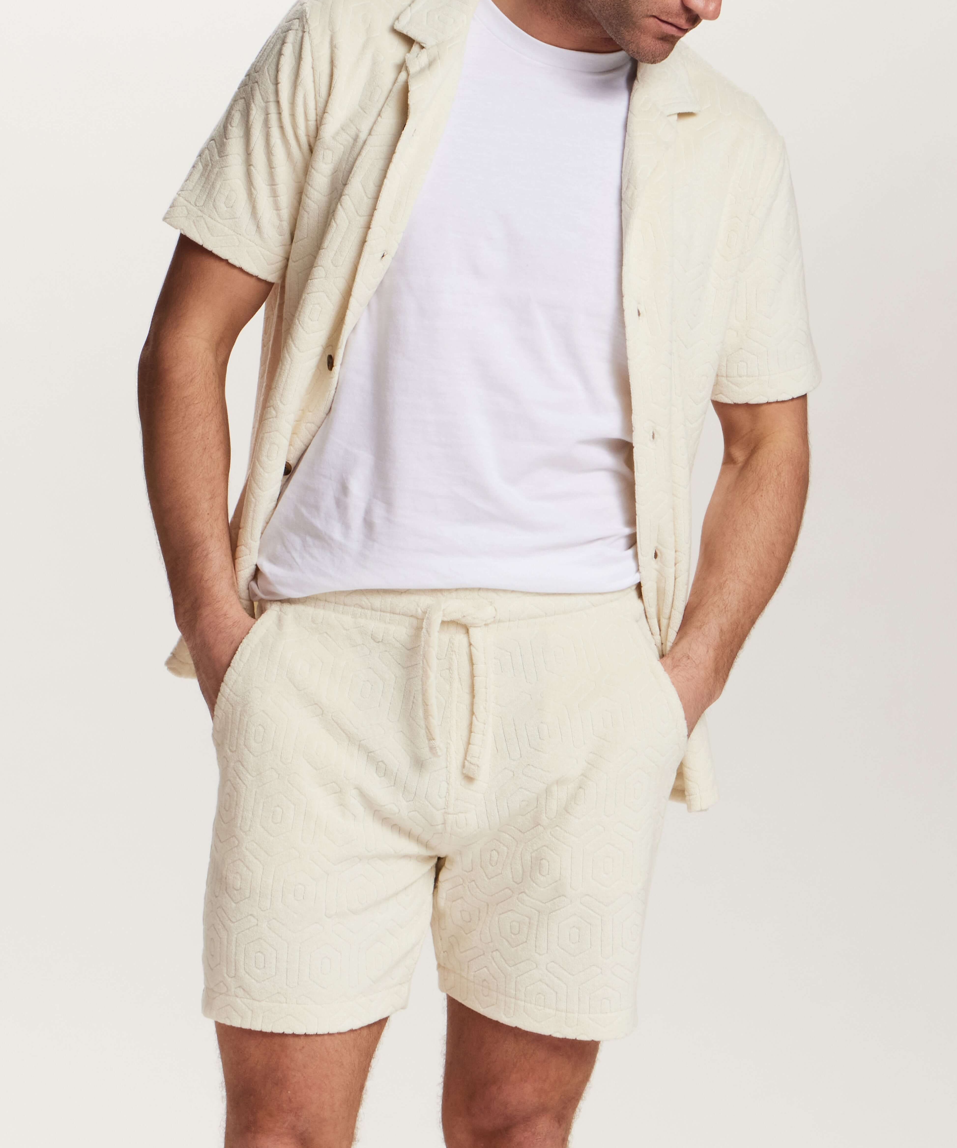 Model wearing Geometric Terry Camp Shirt in Stone, a relaxed button front shirt with geometric pattern and matching shorts.