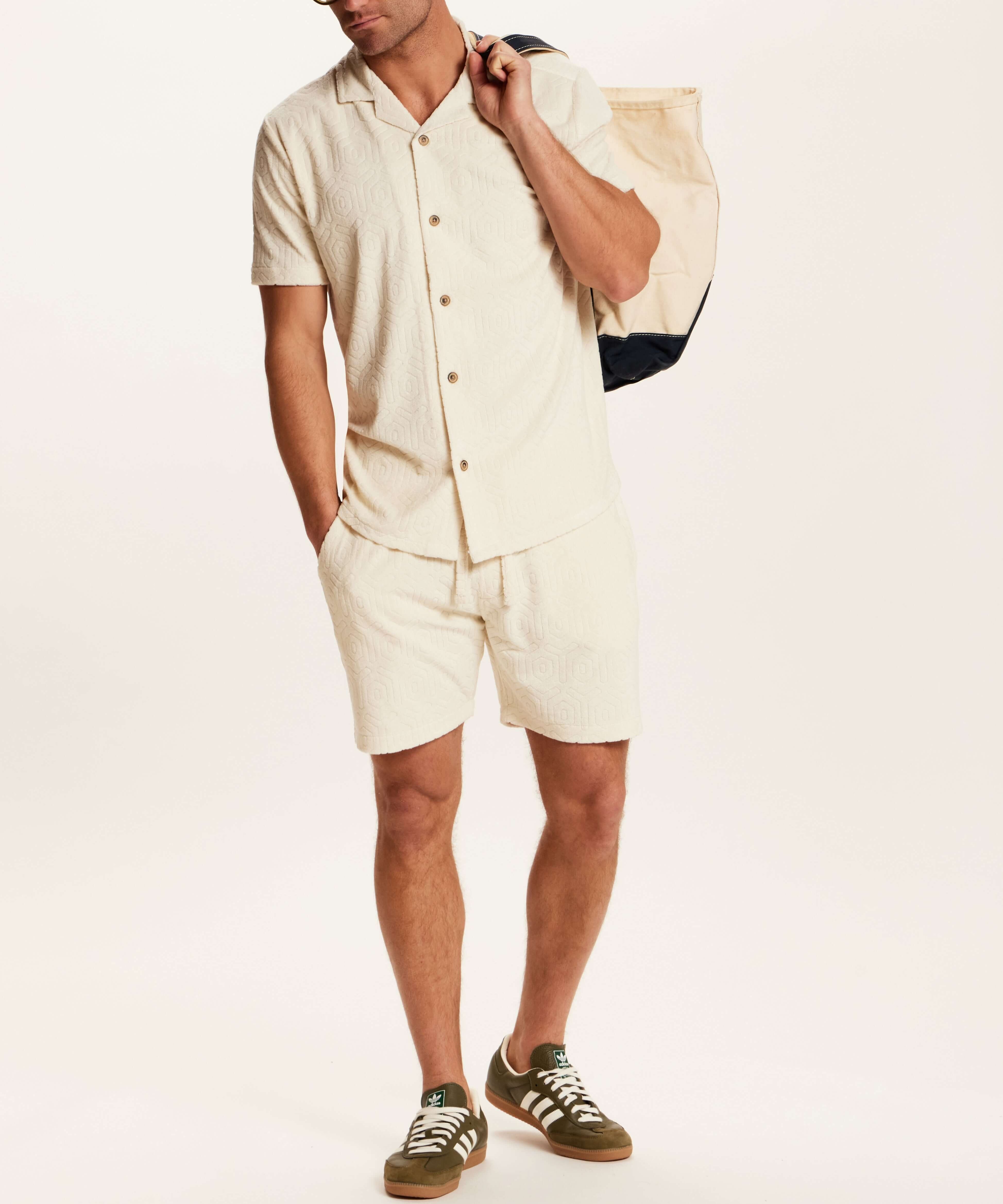 Model wearing the Geometric Terry Drawstring Short in Stone, paired with a matching shirt and carrying a tote.