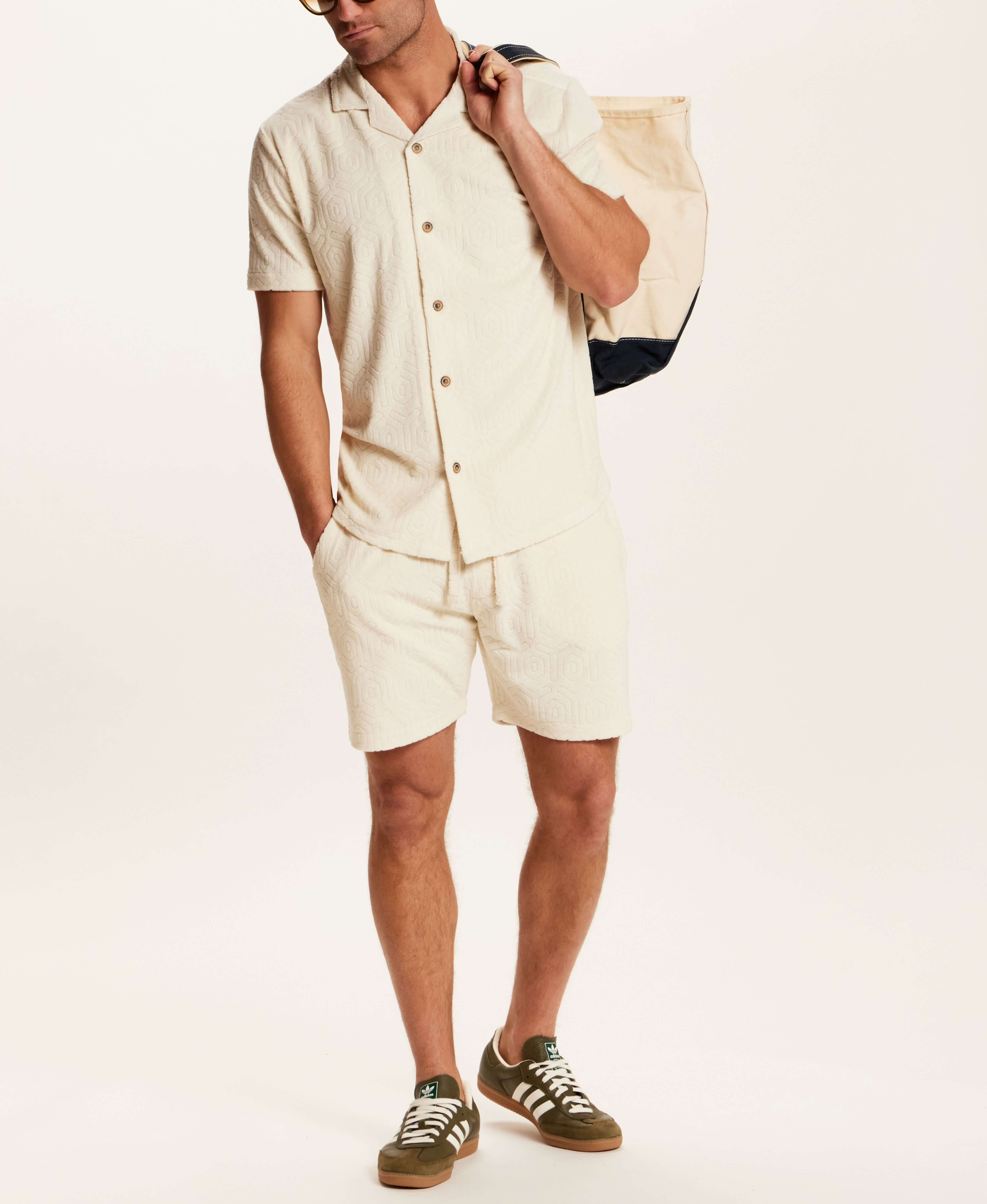 Model wearing the Geometric Terry Drawstring Short in Stone, paired with a matching shirt and carrying a tote.