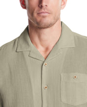 Close-up of a man wearing a Short Sleeve Cotton Linen Airtex Shirt in Sea Grass with a camp collar and button-down pocket.