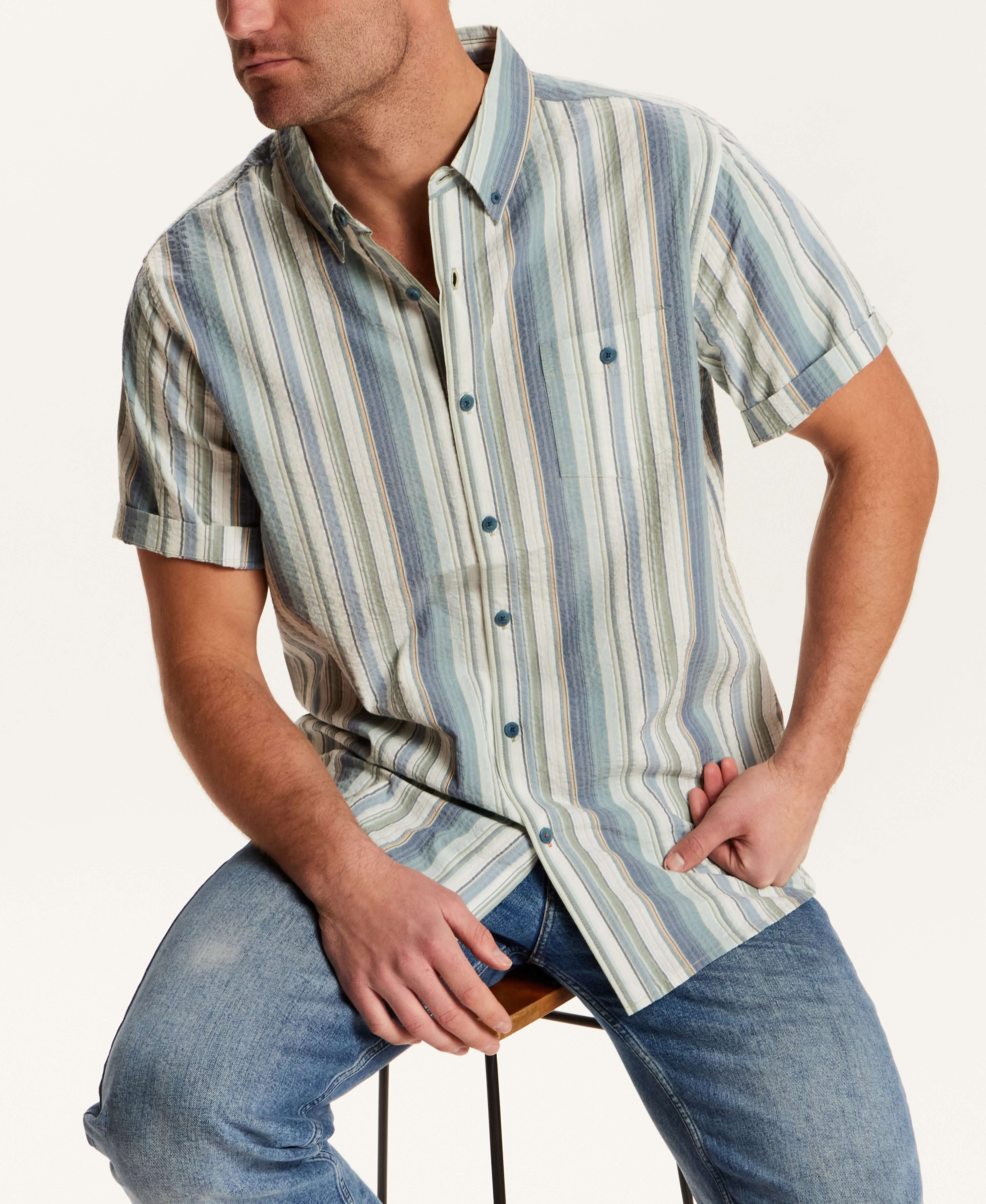 Short Sleeve Seersucker Stripe in Green Slate worn by a model sitting on a chair, showcasing its vertical stripe pattern.