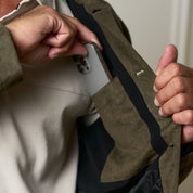 Man placing a phone in the inner pocket of a Sueded Jacket in Olive, showcasing functionality and style.