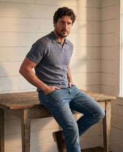 Open Collar Polo Sweater in Sailor Twist model sitting on a rustic table, showcasing comfort and sophistication.