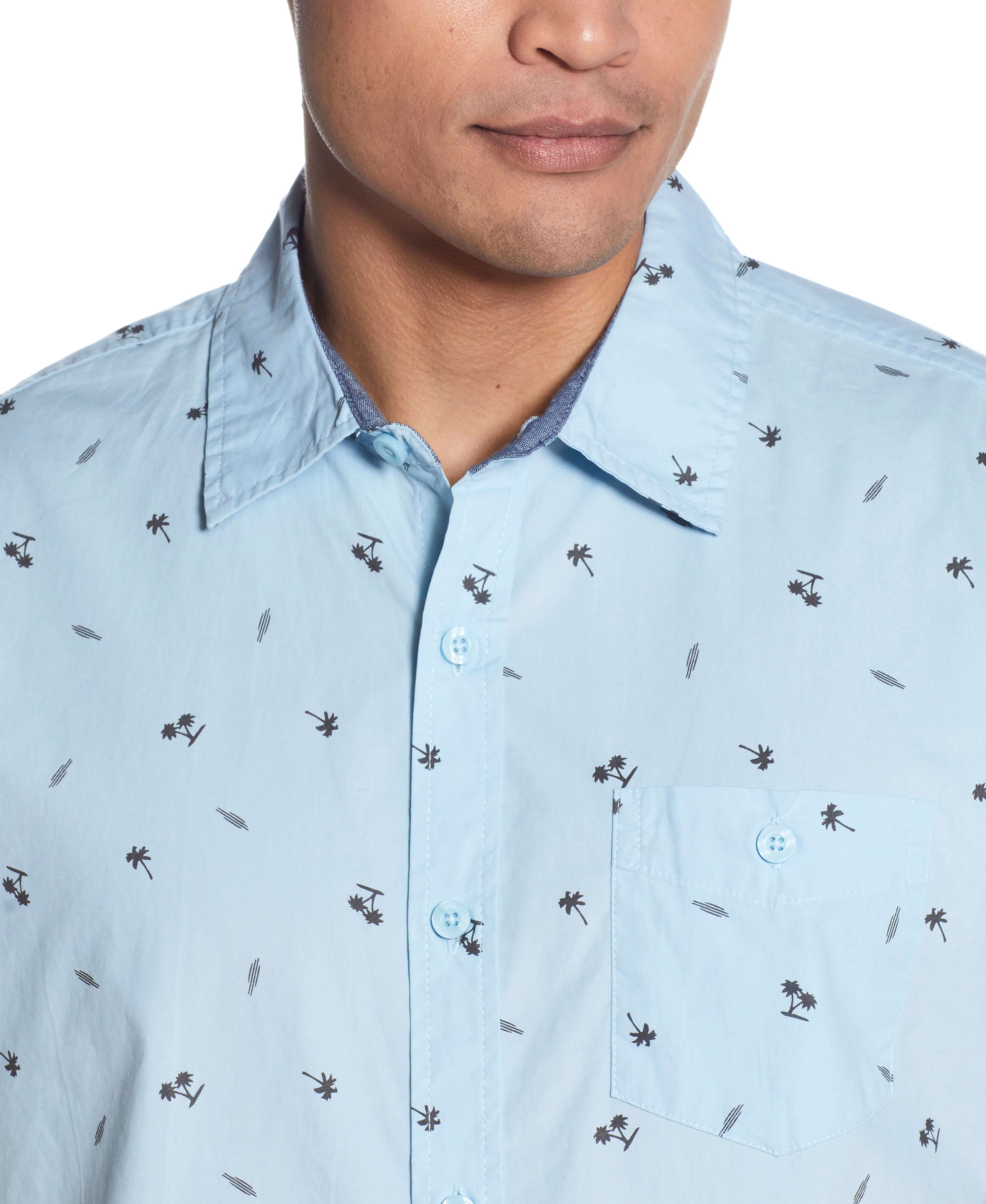 Close-up of a man wearing the Peached Poplin Mini Print In Soft Blue shirt with palm tree print and front pocket.