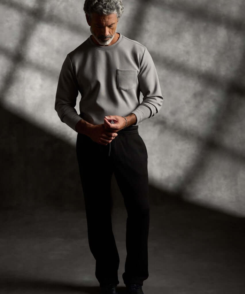 Scuba Crew Neck in Grey worn by a model standing in a shadowy setting, showcasing its modern design and relaxed fit.