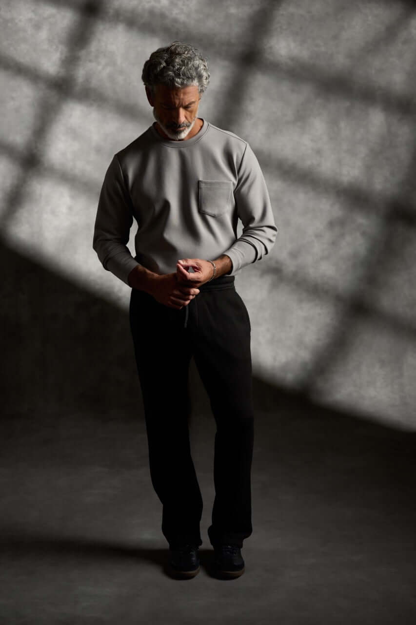 Scuba Crew Neck in Grey worn by a model standing in a shadowy setting, showcasing its modern design and relaxed fit.