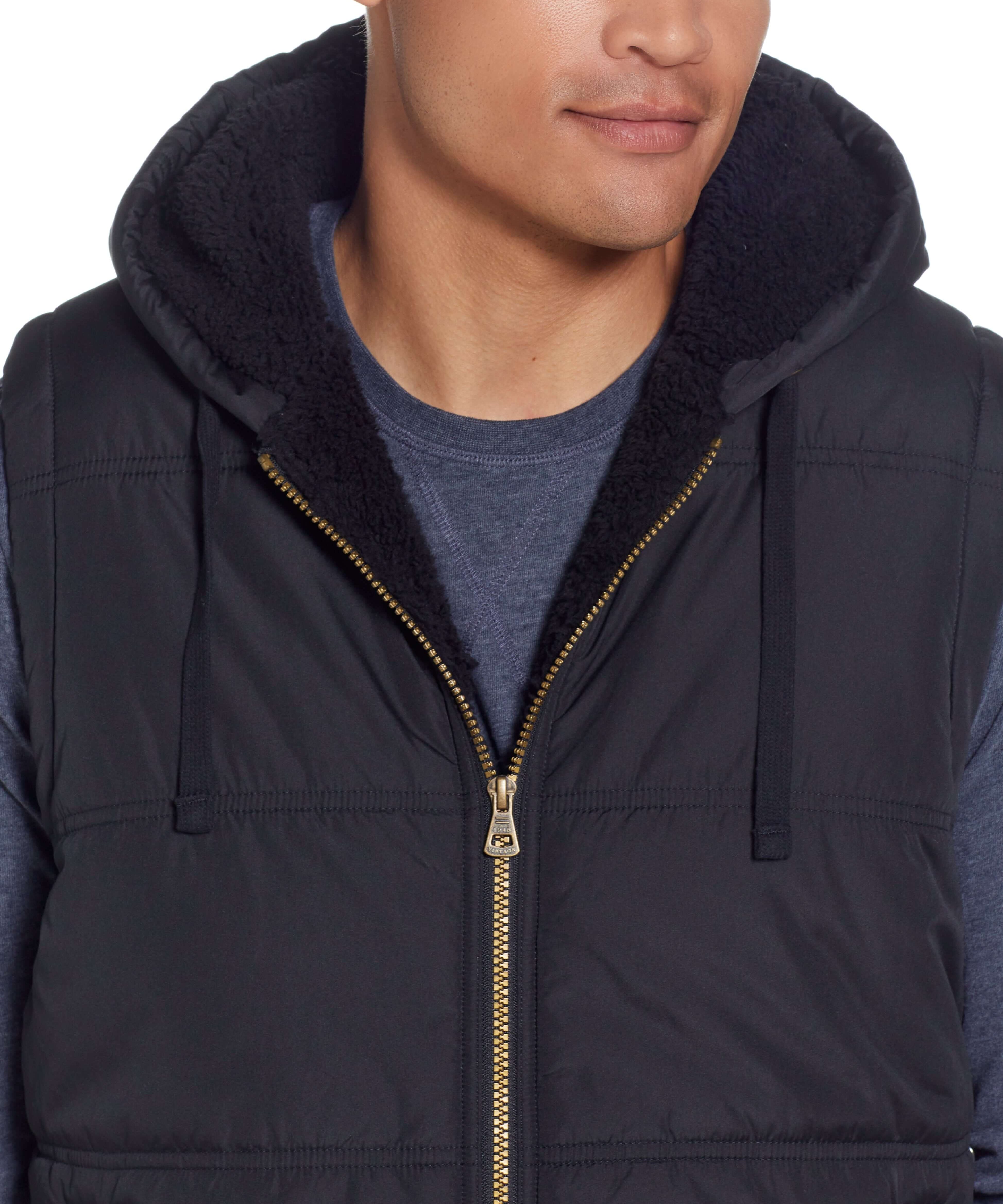 Close-up of man wearing a black Sherpa lined hooded puffer vest with zip front and drawcord hood.