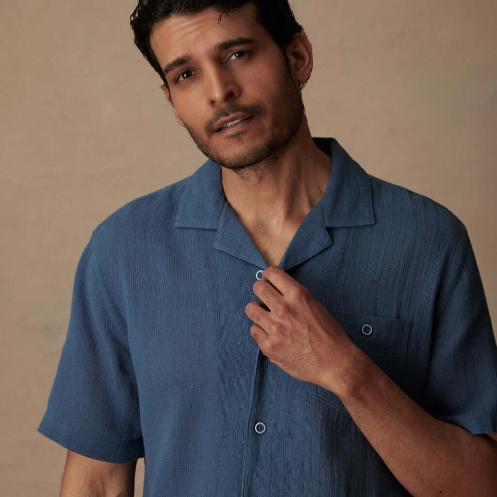 Short Sleeve Cotton Linen Airtex Shirt in Blue Ashes modeled by a man, highlighting its camp collar and button down chest pocket.