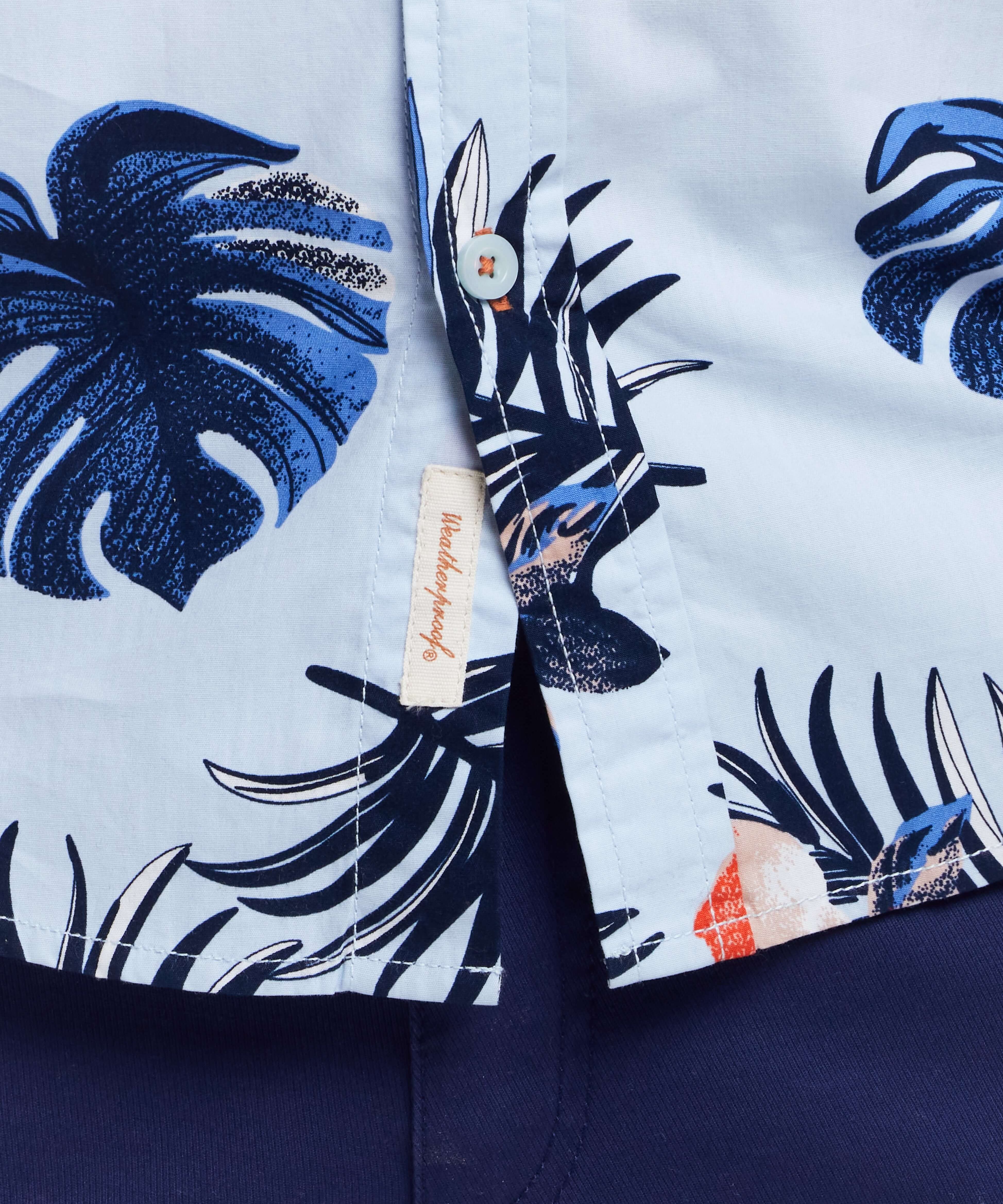 Short sleeve cotton poplin shirt featuring tropical leaves pattern in blue and white, showcasing button-down details.