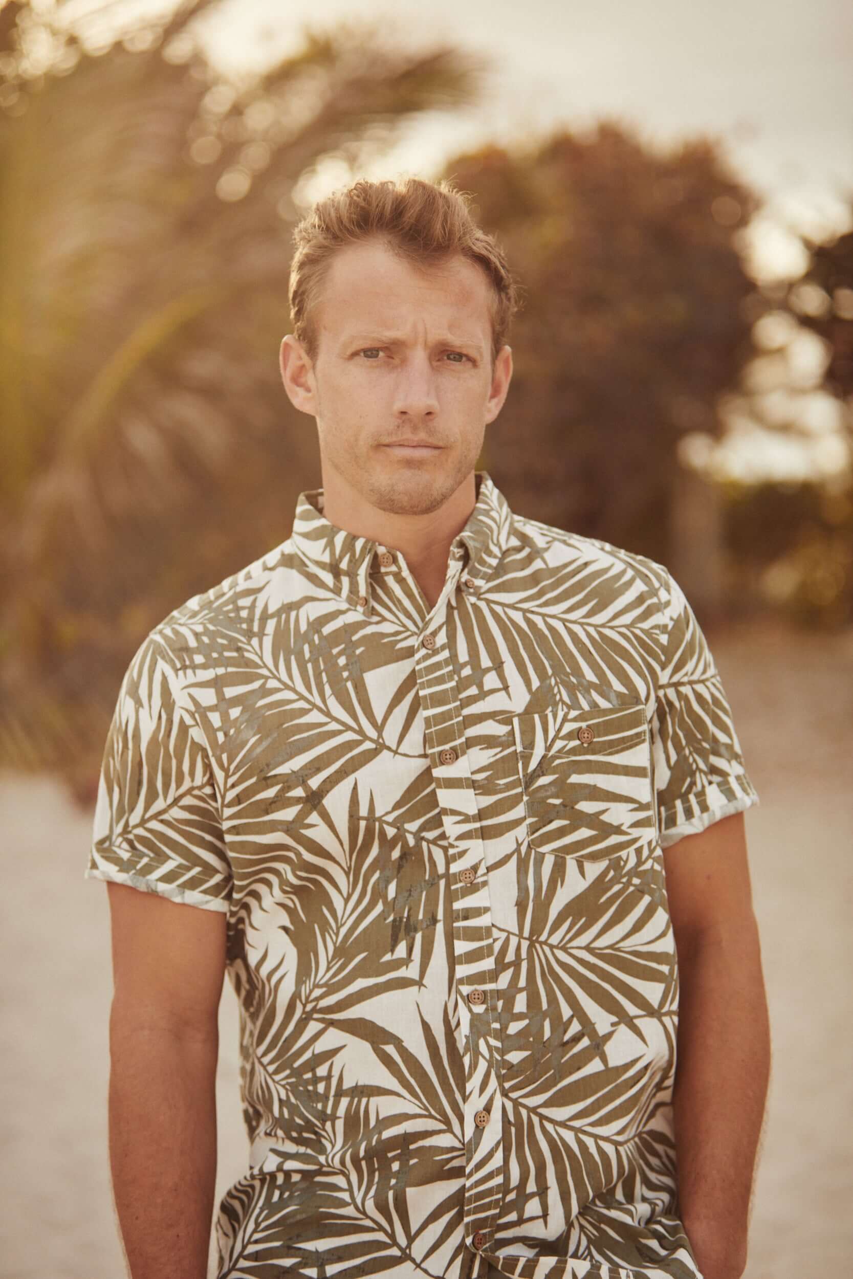 Model wearing a short sleeve floral shirt in lichen green, perfect for casual summer outings.