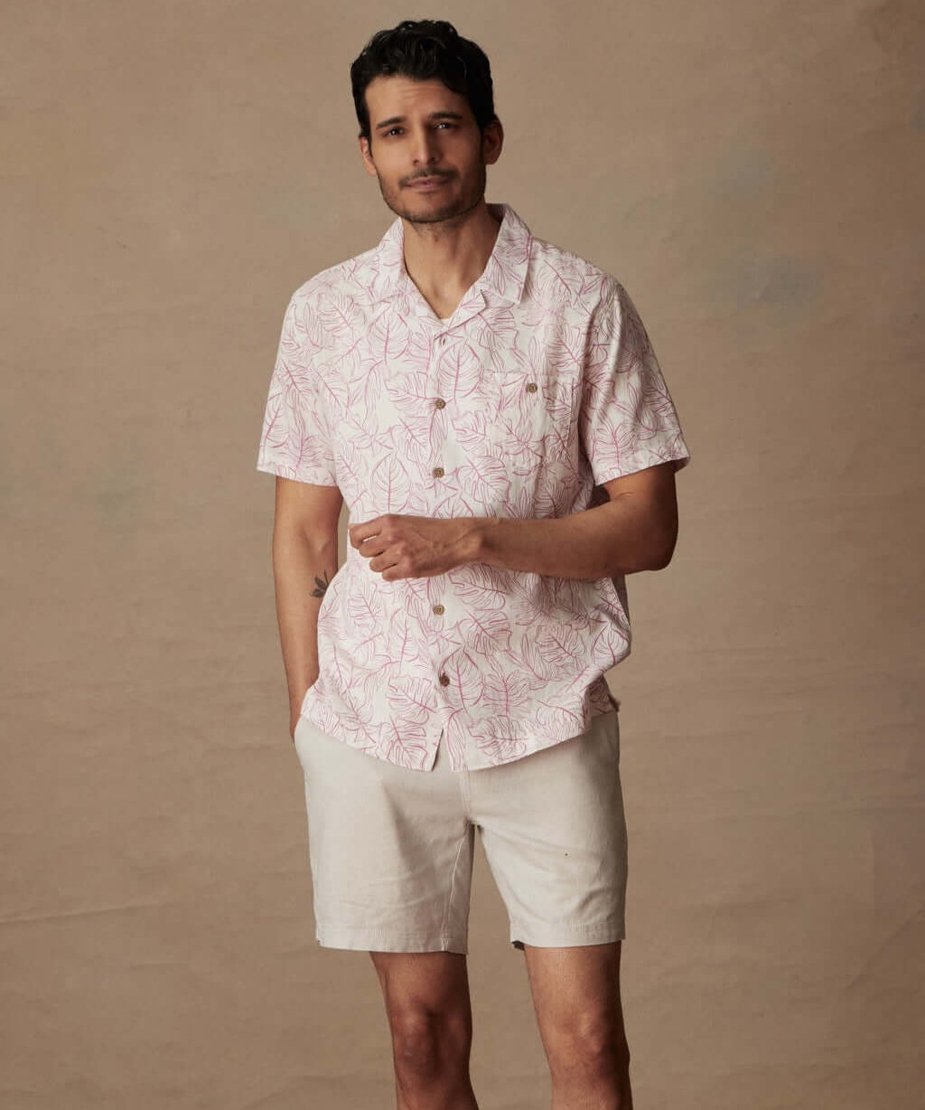 Model wearing a short sleeve linen cotton camp shirt in wild rose with a floral print and shorts.