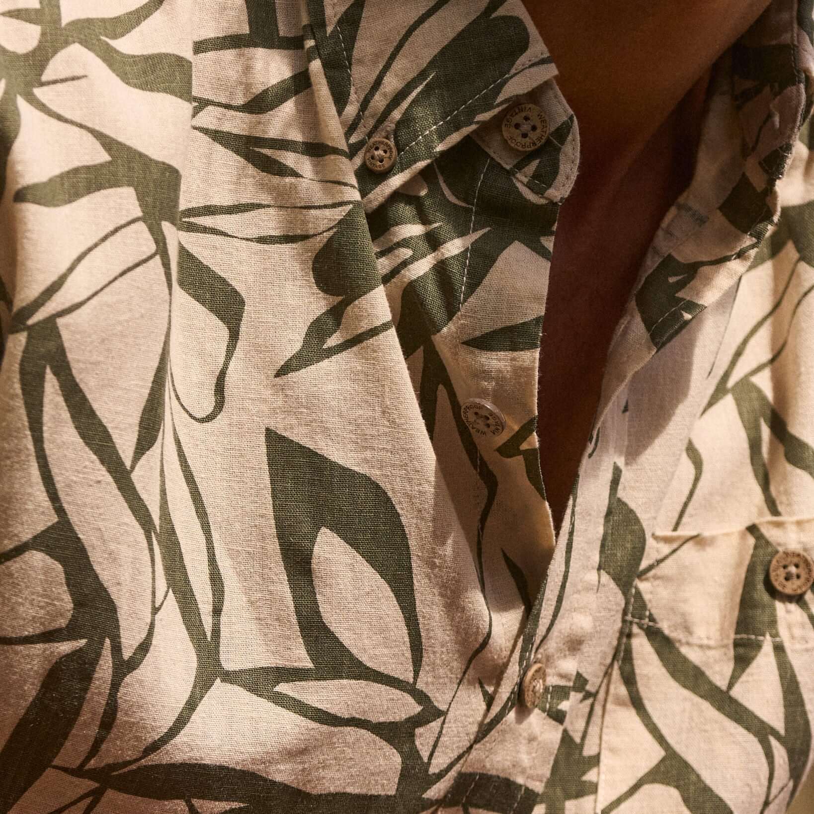 Close-up of a short sleeve linen cotton shirt featuring an abstract four leaf clover print in green and beige.