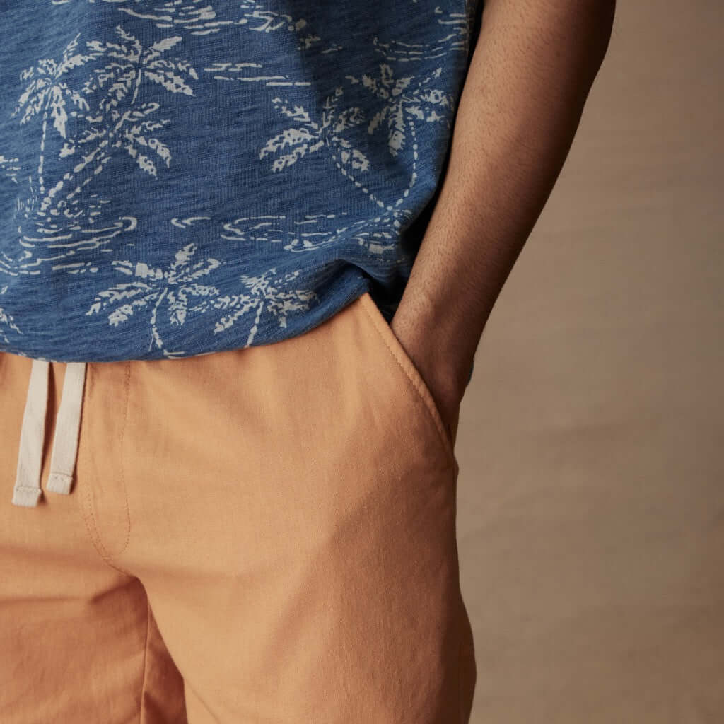 Close-up of a model wearing a dark indigo polo with a tropical print and orange shorts, showcasing a casual style.