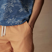 Close-up of a model wearing a dark indigo polo with a tropical print and orange shorts, showcasing a casual style.