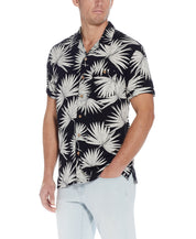 Short Sleeve Rayon Print Camp Collar In Sky Captain worn by a man, featuring a vibrant palm leaf design and button down front.