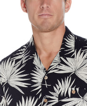 Close-up of a man wearing a Short Sleeve Rayon Print Camp Collar In Sky Captain shirt with palm leaf design.