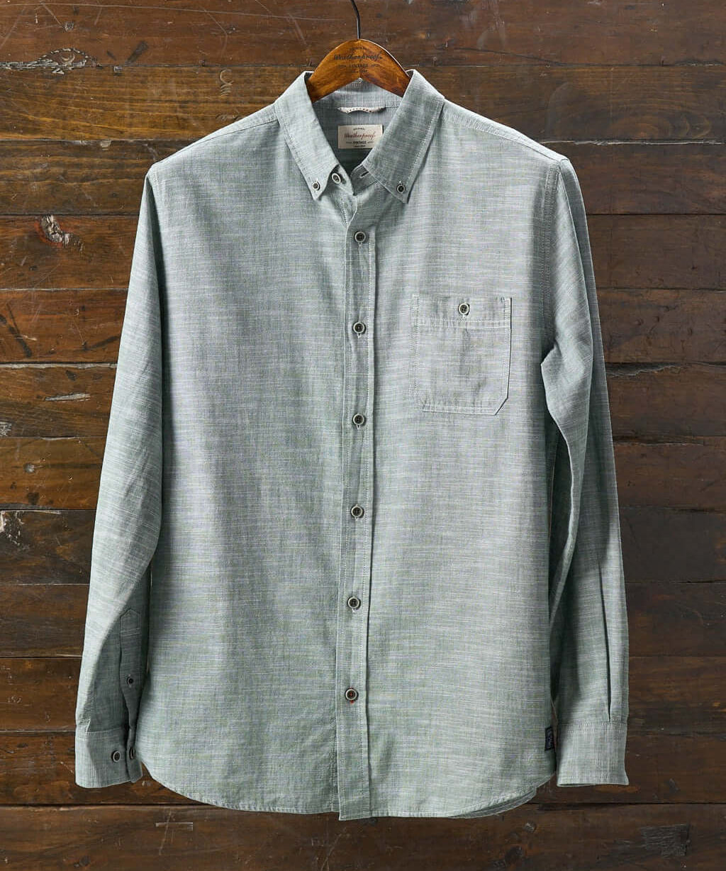 Long sleeve chambray button-down shirt in duck green on a wooden hanger, featuring a chest pocket.