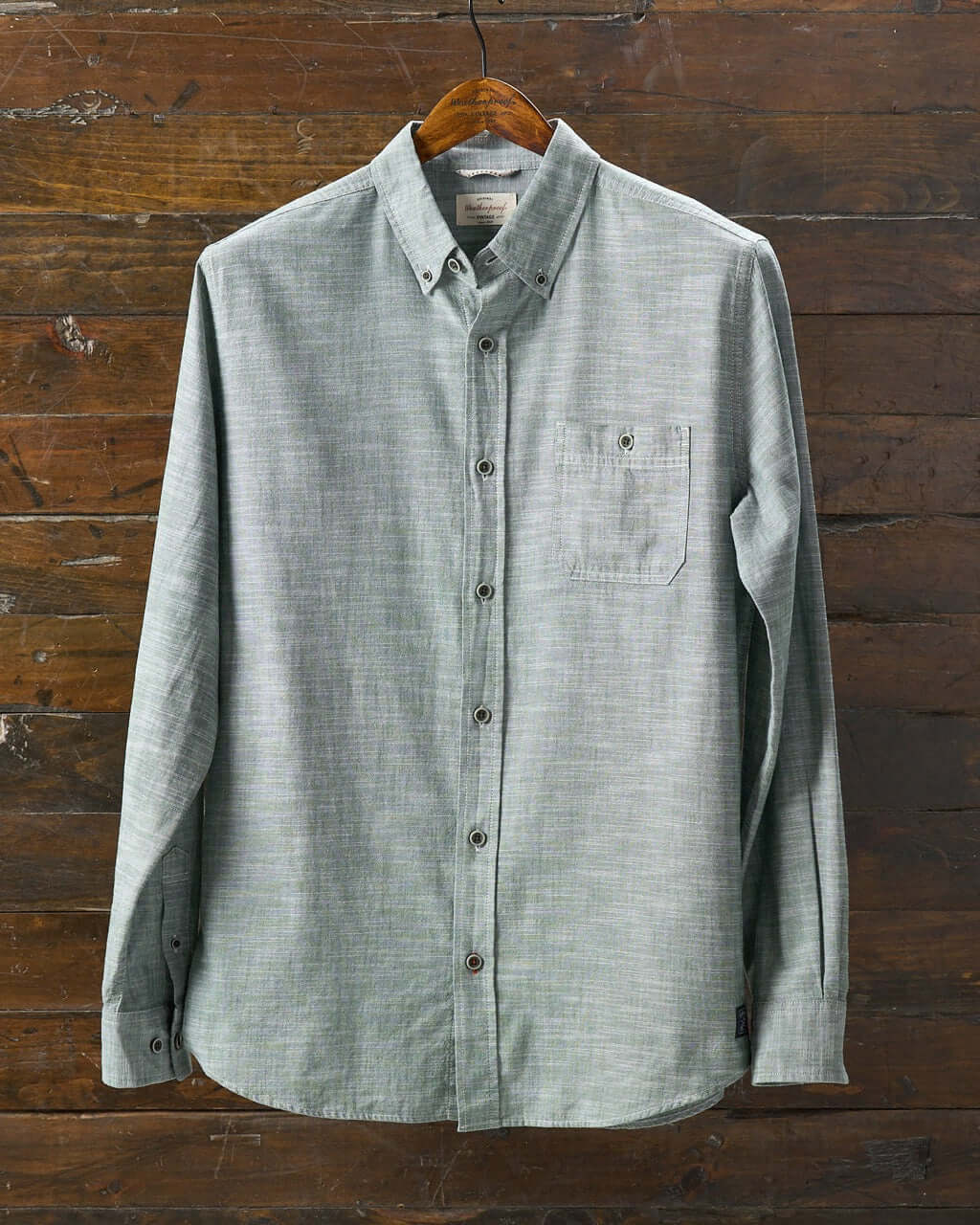 Long sleeve chambray button-down shirt in duck green on a wooden hanger, featuring a chest pocket.