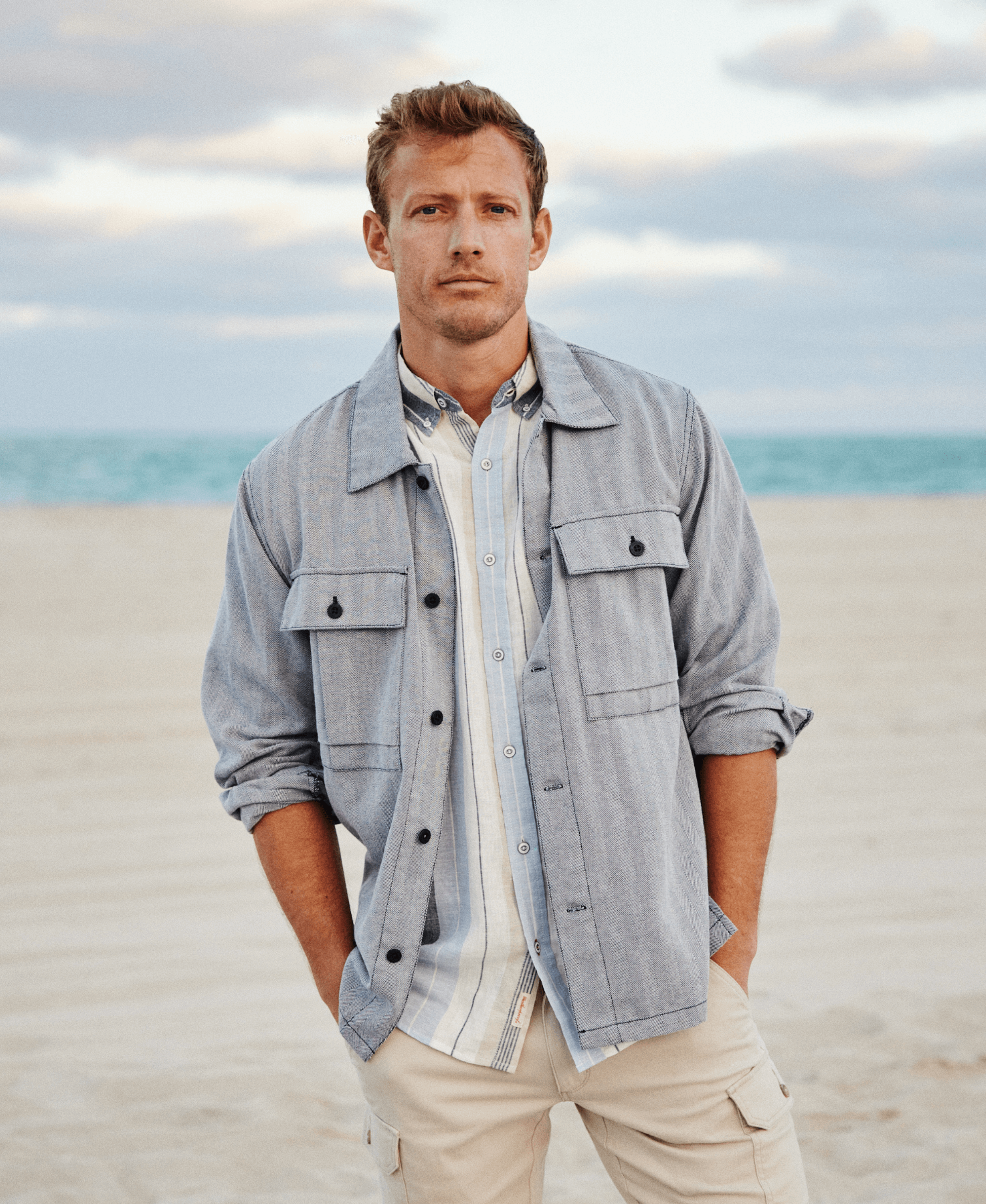 Man wearing a Summer Shirt Jacket In Navy on the beach, showcasing its vintage military-inspired design and patch pockets.
