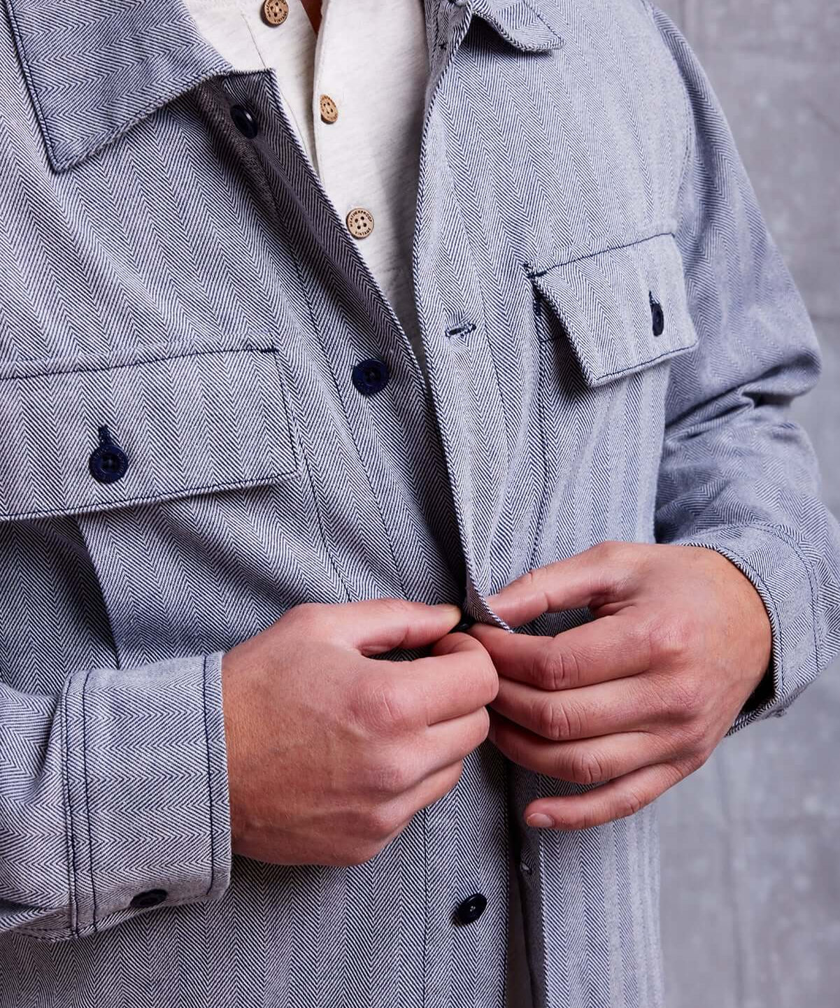 Close-up of a man buttoning a stylish gray shirt jacket over a white henley shirt.