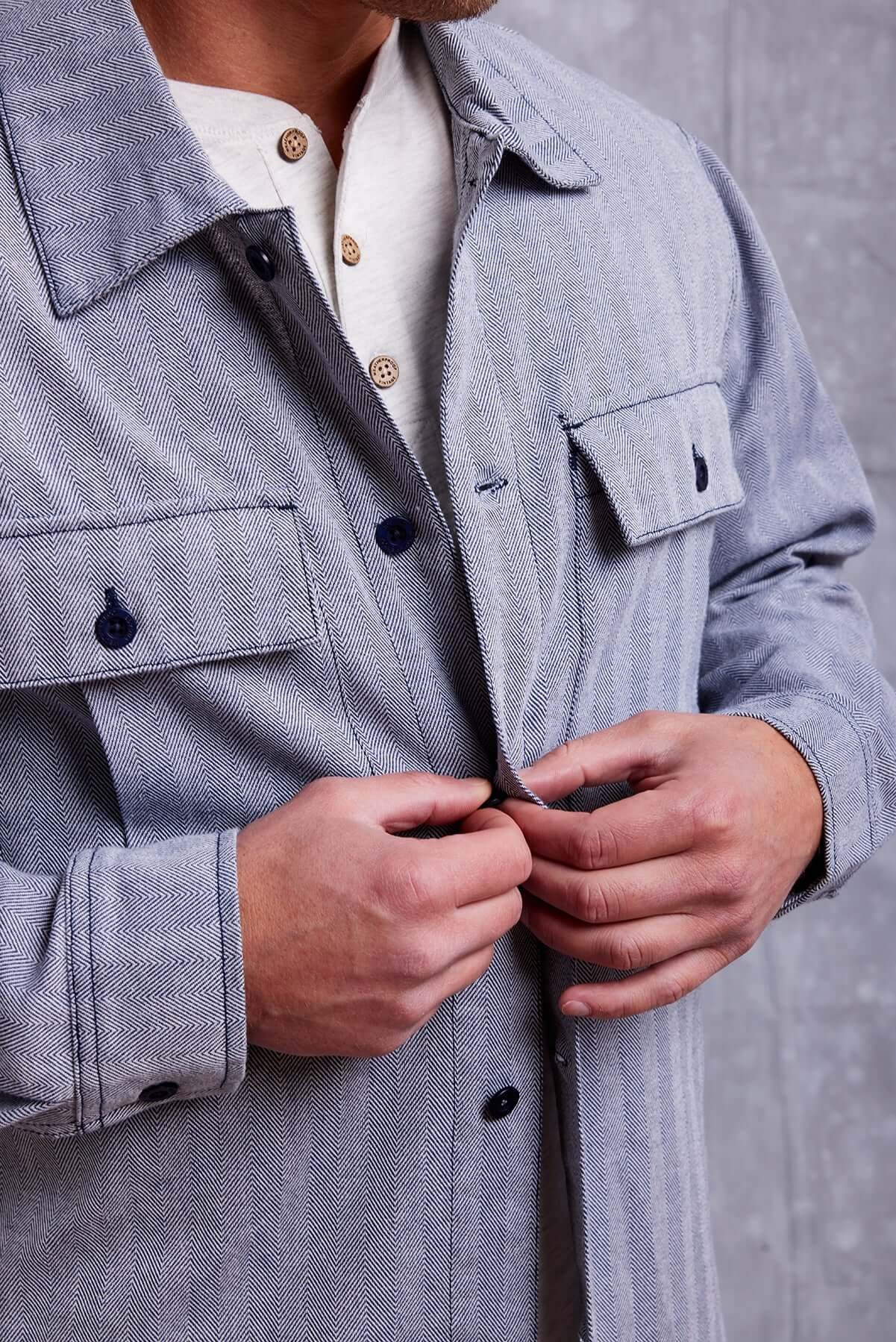 Close-up of a man buttoning a stylish gray shirt jacket over a white henley shirt.