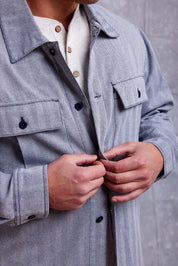 Close-up of a man buttoning a stylish gray shirt jacket over a white henley shirt.